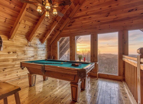 A wooden interior with a pool table, large windows, and a view of the landscape.