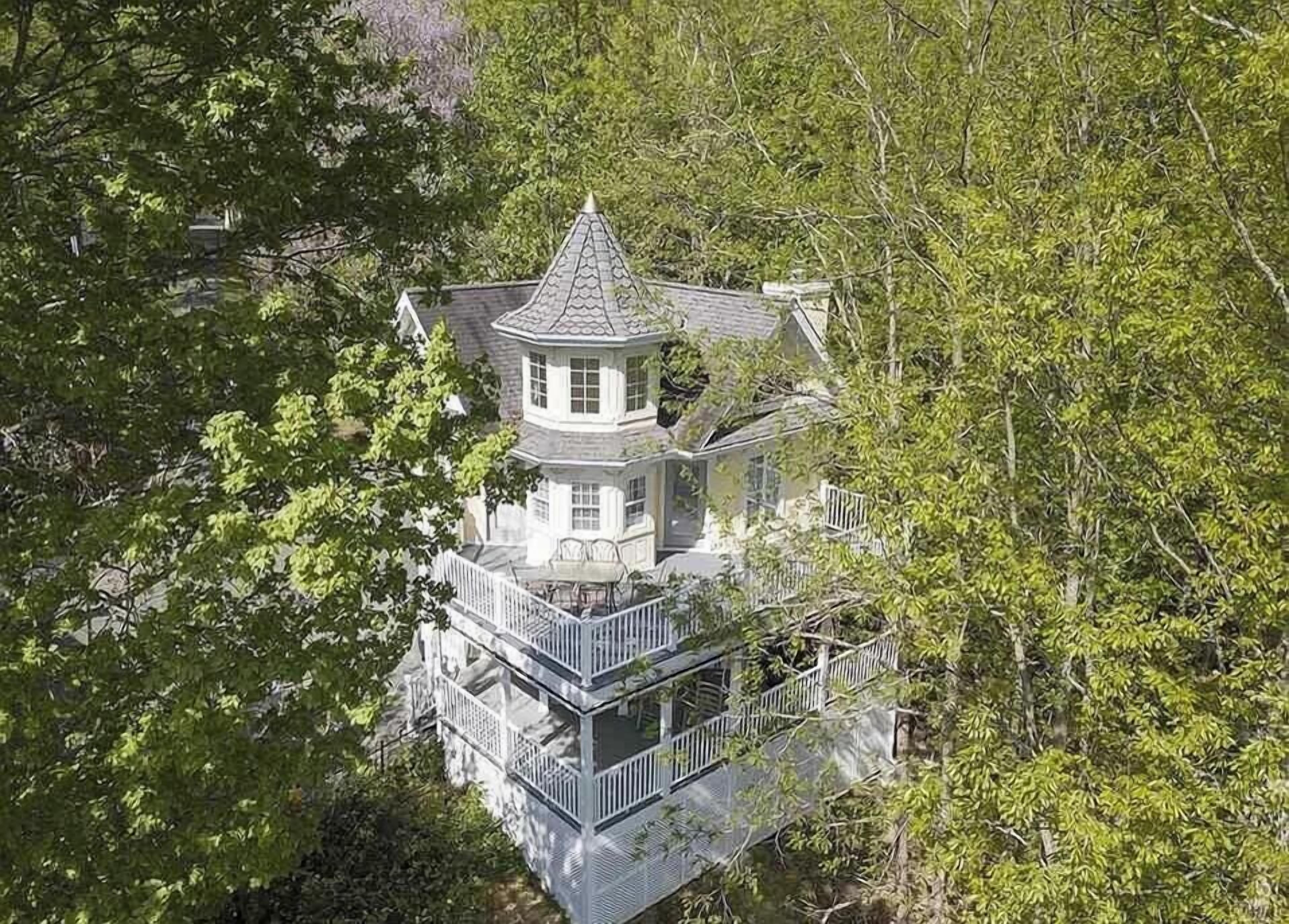 A multi-story house with a tower, surrounded by dense trees.