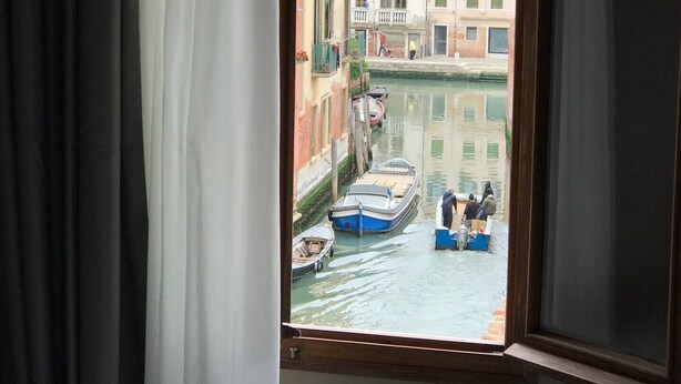A window view of a narrow canal with boats and buildings. - Hotel Cannaregio 2357 (Venice)