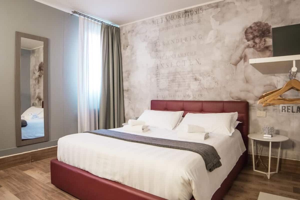 A modern hotel room with a large bed, a mirror, a small round table, and a wall with a textured design.