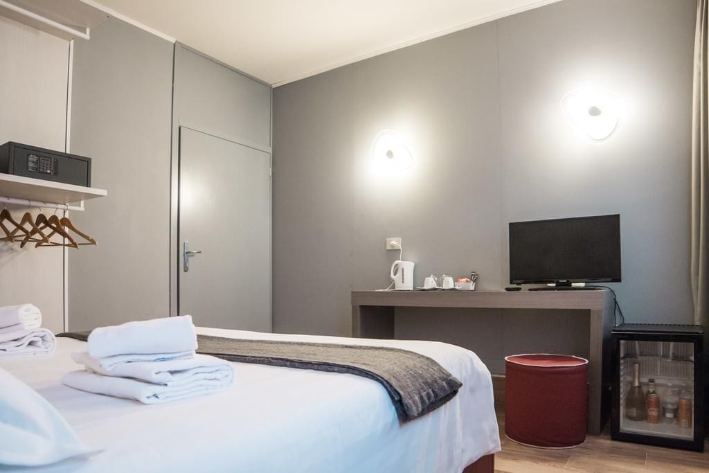 A hotel room with a bed, a television, a minibar, and a red trash bin.