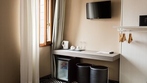 A hotel room with a wooden desk, a flat-screen TV mounted on the wall, a small refrigerator, and a trash bin. - Hotel Cannaregio 2357 (Venice)