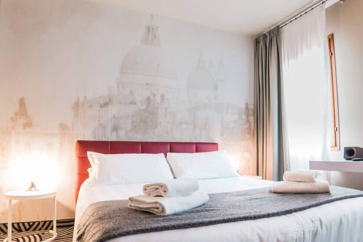 A hotel room with a bed, a nightstand, a lamp, and a wall with a cityscape mural.