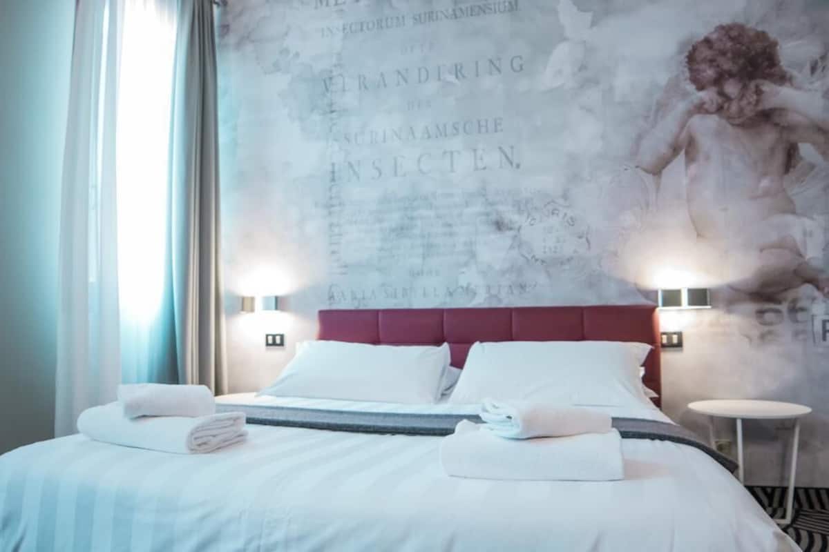 A hotel room with a large bed, two bedside tables, and a wall with a historical painting.