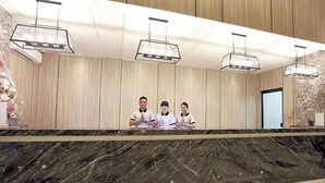 A reception desk with a marble countertop, wooden panel walls, and pendant lighting. - Grand Karlita Purwokerto (Purwokerto)