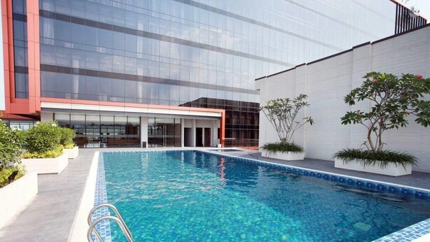 A modern building with a glass facade, a swimming pool with blue mosaic tiles, and potted plants. - Grand Karlita Purwokerto (Purwokerto)