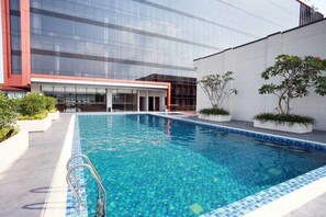 A modern building with a glass facade, a swimming pool with blue mosaic tiles, and potted plants. - Grand Karlita Purwokerto (Purwokerto)