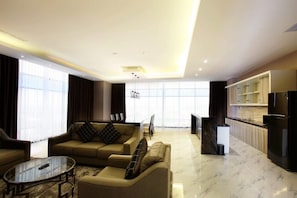 A modern living room with a sofa set, a coffee table, and a kitchen area with a refrigerator and cabinets. - Grand Karlita Purwokerto (Purwokerto)
