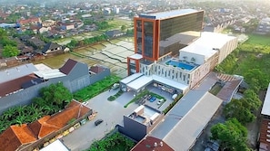 A modern building with a large glass facade, a swimming pool, and a parking area. - Grand Karlita Purwokerto (Purwokerto)