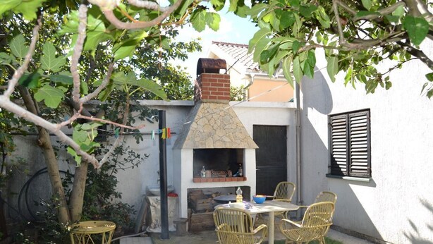Eine Terrasse mit Korbstühlen und einem Tisch, einem Backofen aus Ziegelsteinen und einer weißen Wand mit Fensterläden.