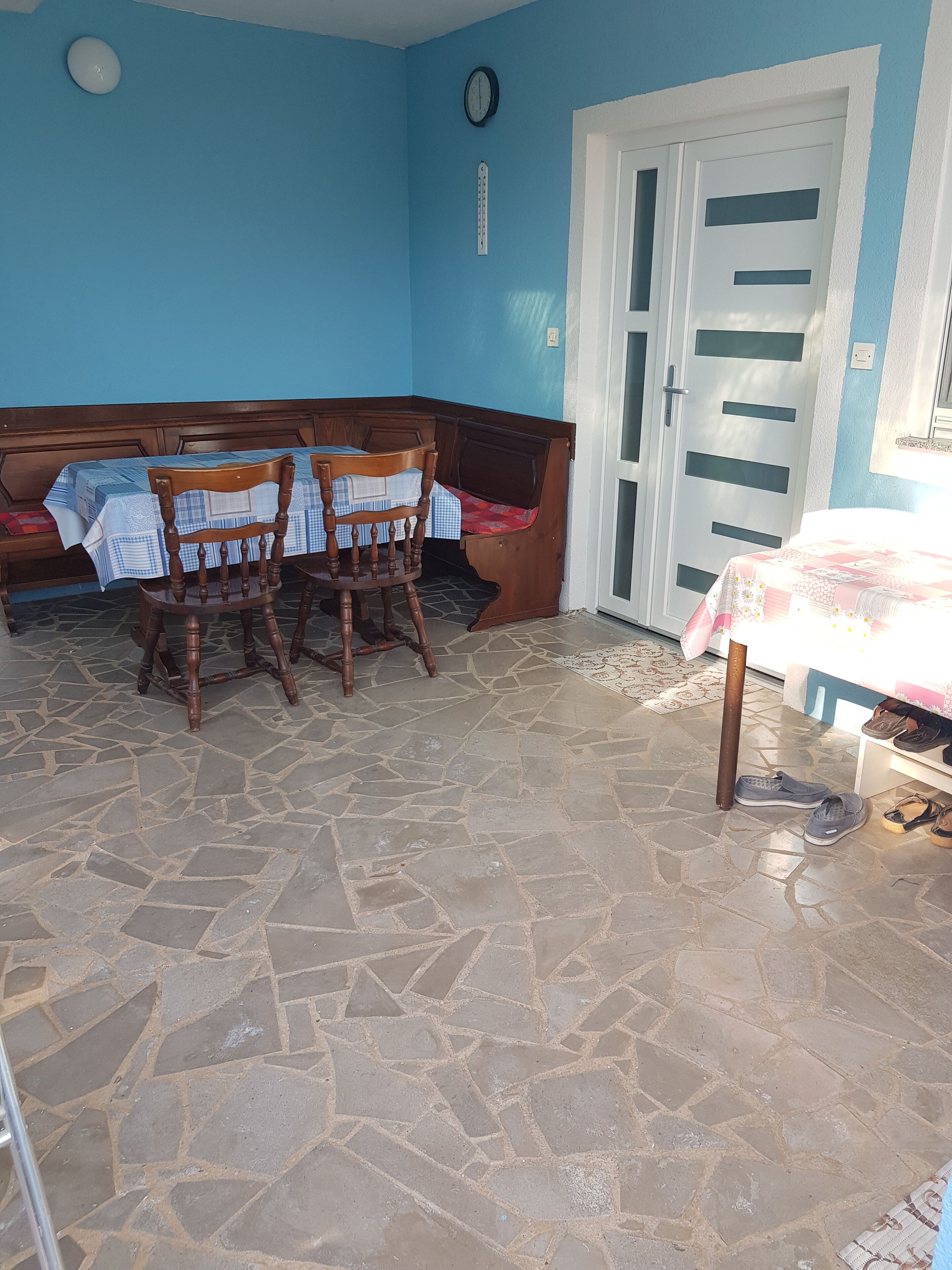 Una habitación con suelo de piedra, un banco de madera, una mesa con mantel y una puerta con ventana.