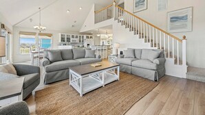 A spacious living room with a large gray sectional sofa, a coffee table, and a staircase leading to an upper level. - Why Knot 4 bedroom in The Currituck Club (Corolla)