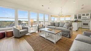 A spacious living room with a large sofa, two armchairs, a coffee table, and a view of the outdoors through large windows. - Why Knot 4 bedroom in The Currituck Club (Corolla)