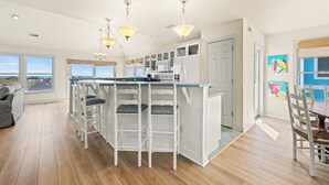 A modern kitchen with a central island, bar stools, pendant lighting, and a view of the sea. - Why Knot 4 bedroom in The Currituck Club (Corolla)