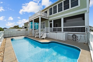 A swimming pool with a covered deck area, a white picket fence, and a two-story building with a balcony. - Why Knot 4 bedroom in The Currituck Club (Corolla)