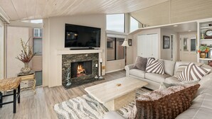 A spacious living room with a fireplace, a large flat-screen TV, and a comfortable seating area with a sofa and armchairs. - Sea For Miles Top Floor Oceanfront Rental - A/C, Beach Access, Pool (Solana Beach)