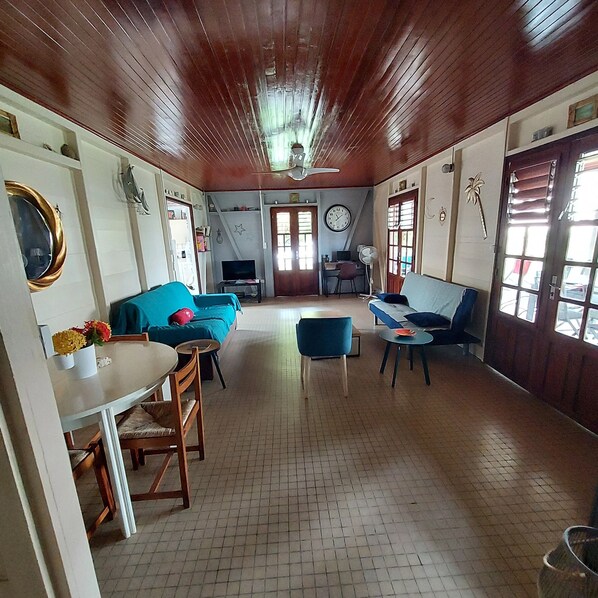 A spacious room with a wooden ceiling, a sofa, a dining table, and a TV. - Spacious Creole villa, in the heart of Saint-François (SAINT FRANCOIS)
