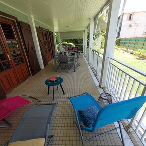 A covered outdoor area with a tiled floor, a table with chairs, and a blue chair with a cushion. - Spacious Creole villa, in the heart of Saint-François (SAINT FRANCOIS)