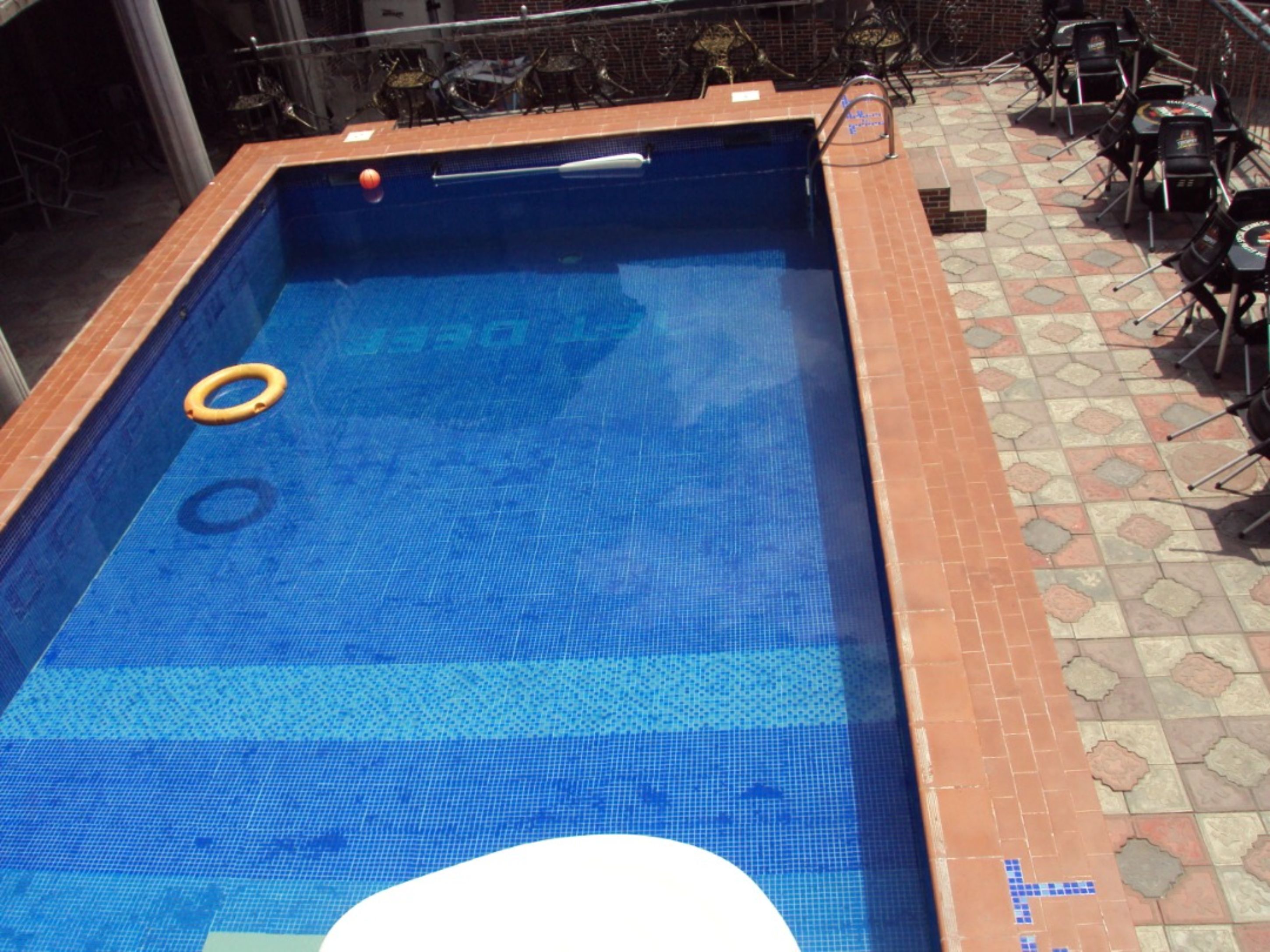 Una piscina rectangular con borde de azulejos, rodeada por una zona de patio con sillas y una mesa.
