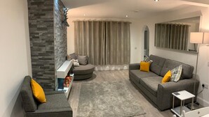 Una sala moderna con un sofá y un sillón grises, una pared de acento de piedra, un tapete gris y un espejo sobre el sofá.