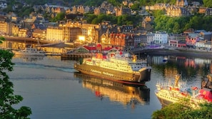 A large cruise ship named Caledonian MacBrayne docked at a port with a cityscape in the background.