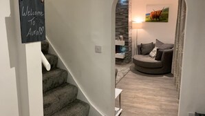 Un interior moderno con una escalera que conduce a una sala de estar con un muro de acento de piedra, un sofá y una lámpara.