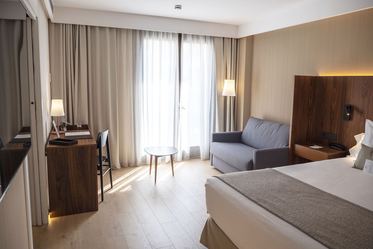 Habitación de hotel con cama, escritorio, silla, sofá, mesita y lámpara.