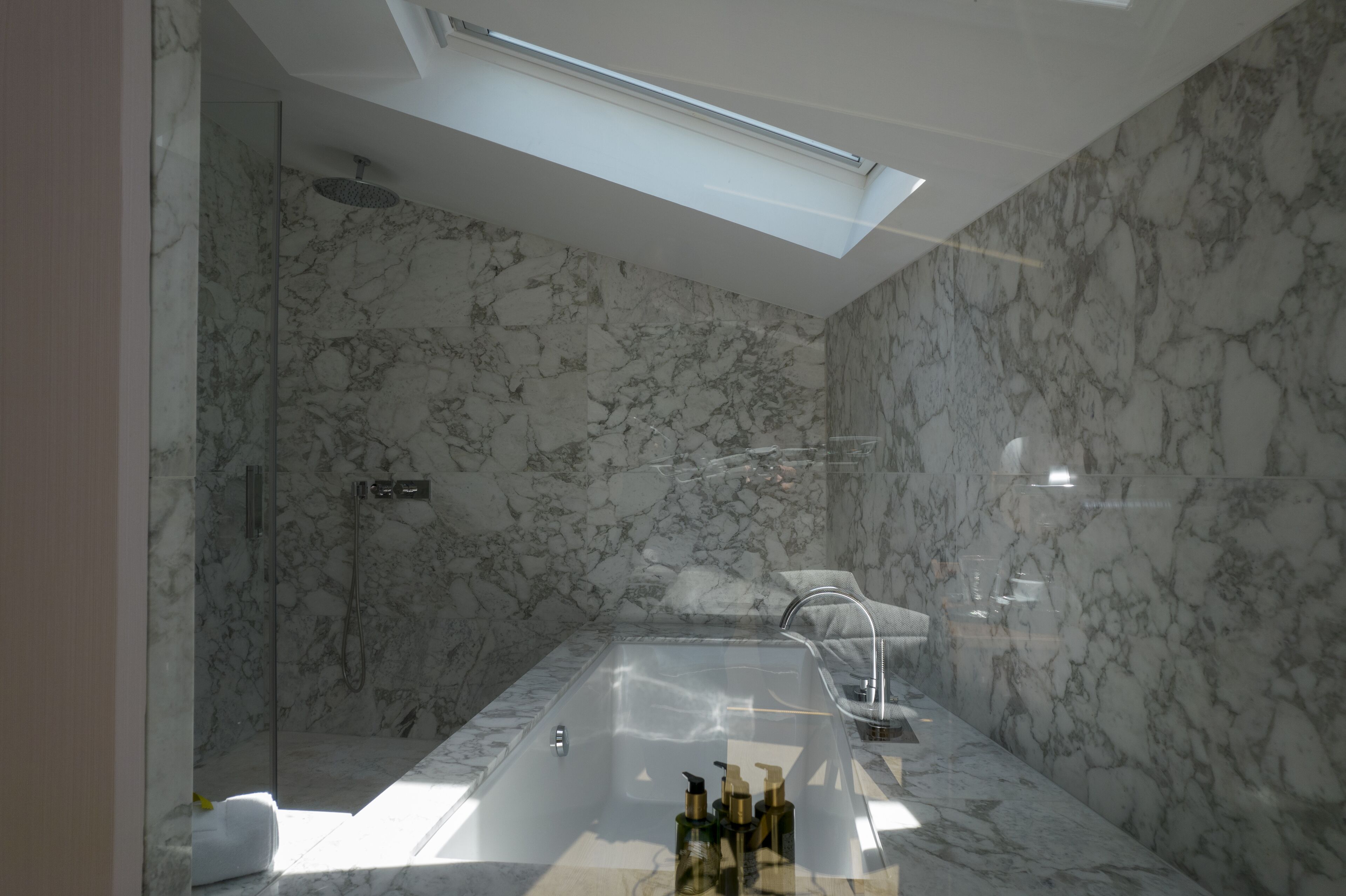A modern bathroom with a glass-enclosed shower, a large bathtub, and marble walls.