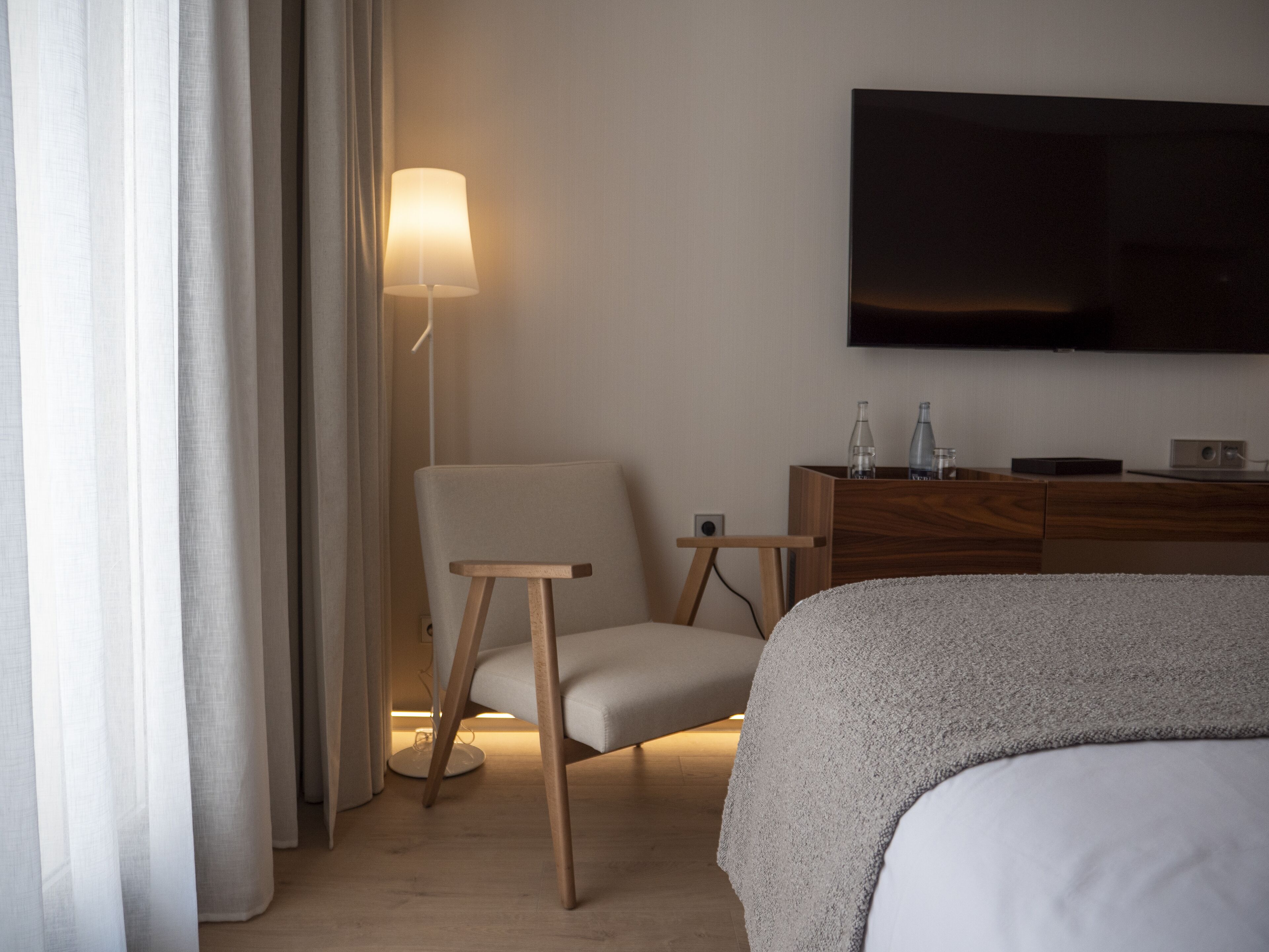 Habitación de hotel con cama, una silla, mesita de noche, lámpara y televisor de pantalla plana montado en la pared.