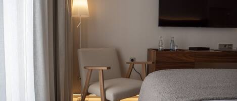 Habitación de hotel con cama, una silla, mesita de noche, lámpara y televisor de pantalla plana montado en la pared.
