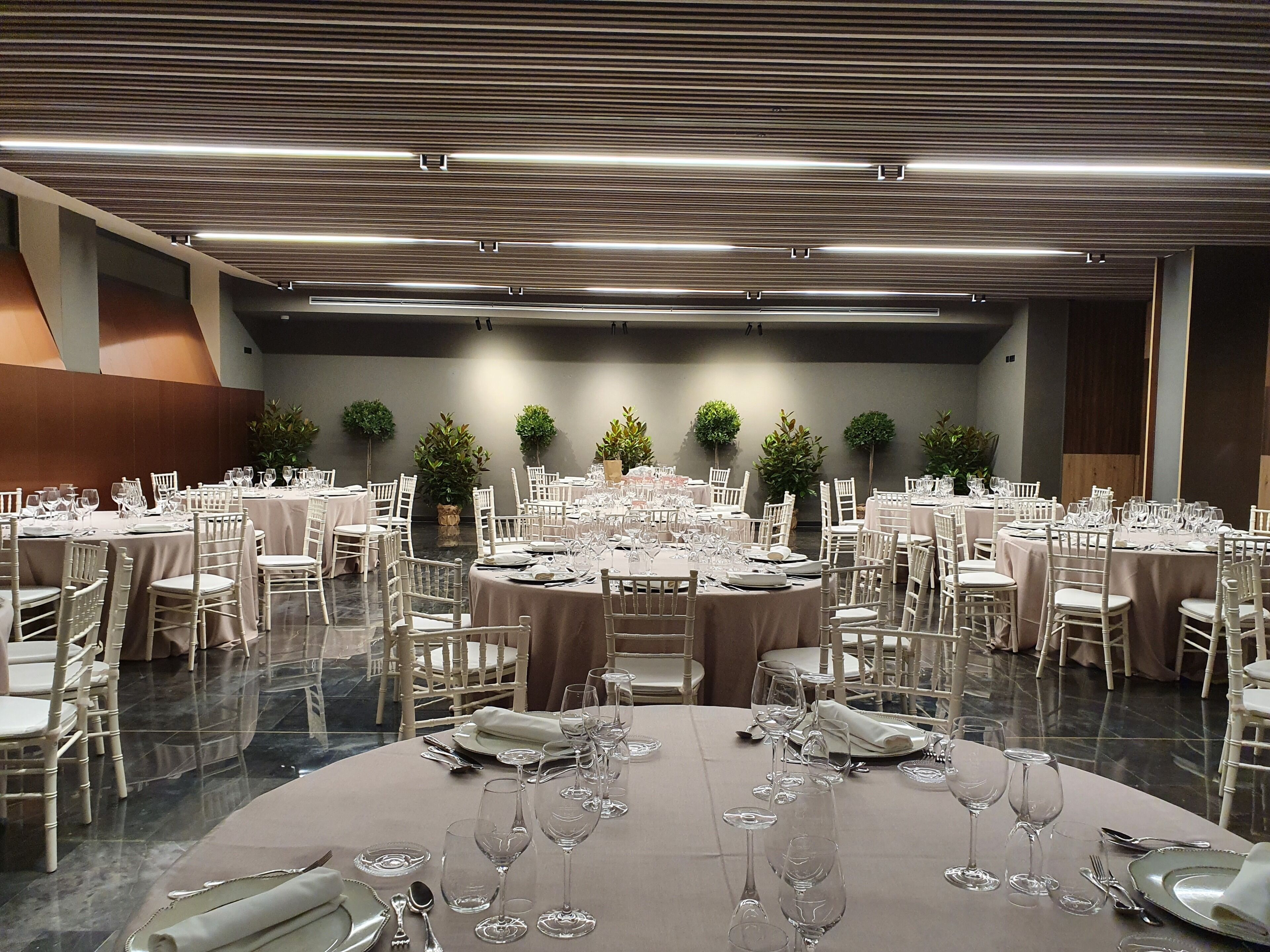 Un salón de banquetes con varias mesas redondas dispuestas para cenar, rodeado de sillas blancas.