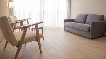 Un moderno salón con un sofá gris, sillas de madera y una mesa de centro de vidrio.