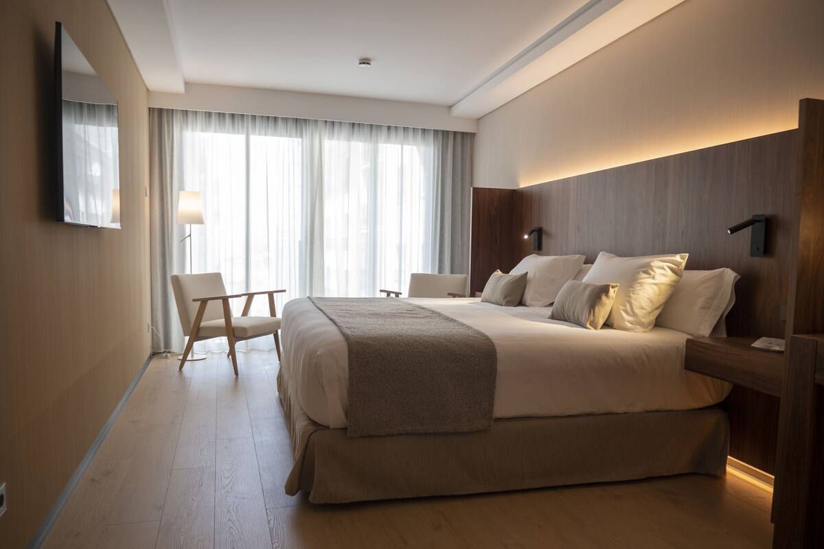 Habitación de hotel con una cama grande, un escritorio, una silla, un televisor y una ventana con cortinas.