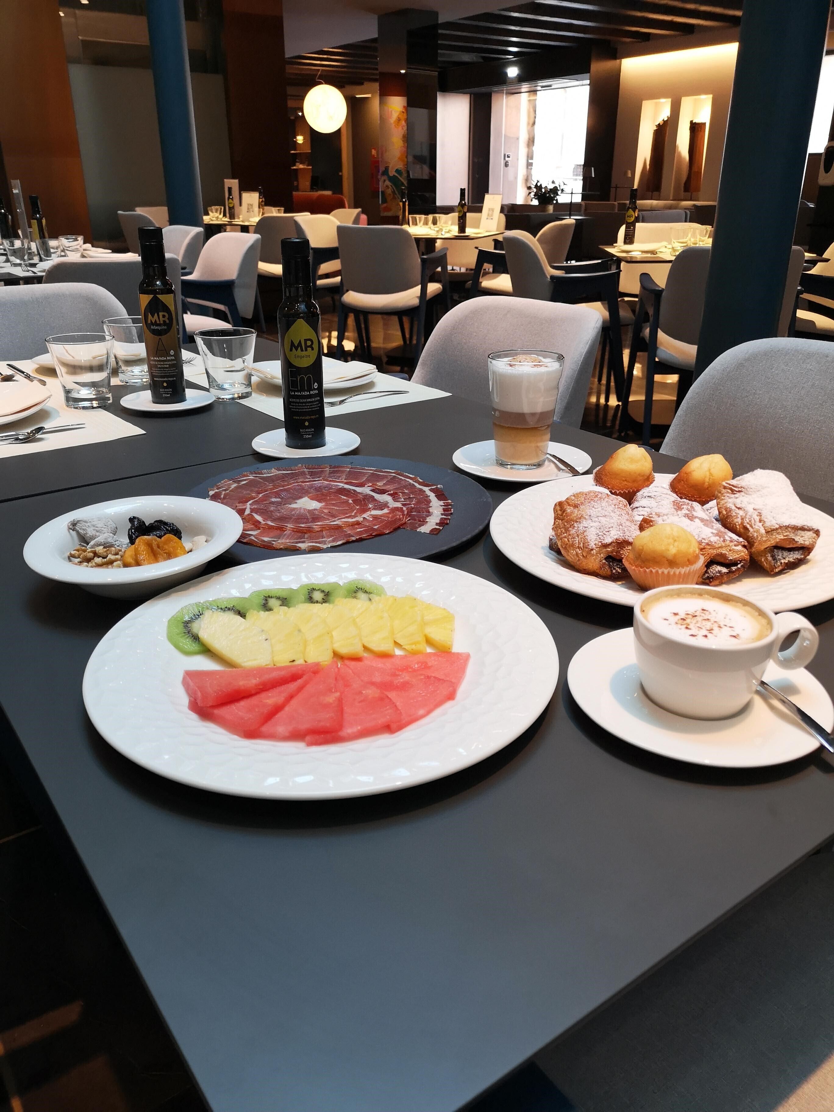 Una mesa de comedor dispuesta con platos de fruta, pasteles y una botella de vino.