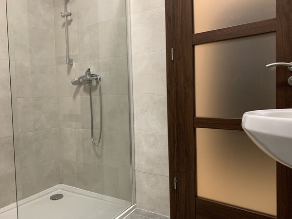 A shower with a glass door, a wooden door frame, and a white sink.
