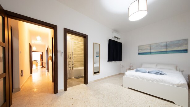 A bedroom with a bed, a nightstand, a wall-mounted air conditioner, and a painting. - Large 3bedroom apartment near rocky beach MCRE1-1 (Sliema)