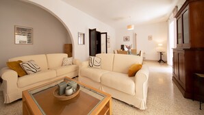 A spacious living room with two cream-colored sofas, a glass coffee table, and a wooden cabinet. - Large 3bedroom apartment near rocky beach MCRE1-1 (Sliema)