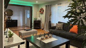Una sala de estar moderna con un sofá oscuro, una mesa de centro y un comedor con un banco y una mesita.