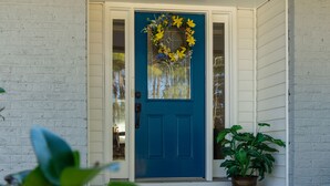 Una puerta azul adornada con un lazo de laurel, una planta en maceta y un felpudo.