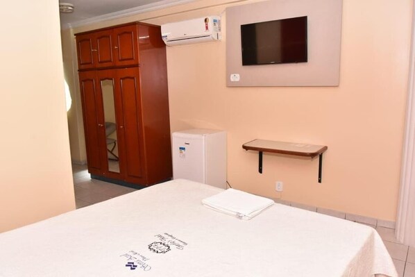 A bedroom with a bed, a wardrobe, a TV mounted on the wall, and a small shelf. - Serra Azul Plaza Hotel (Barra do Garcas)