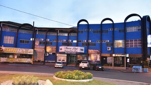 Un hotel con facciata blu, diverse unità di condizionamento e un'aiuola davanti.