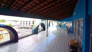 Un'area esterna coperta con pavimento piastrellato, una parete blu e vista su un parcheggio e edifici sullo sfondo.