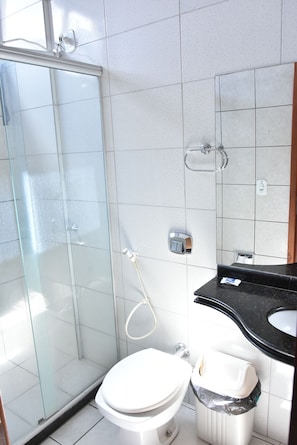 A bathroom with a glass-enclosed shower, a white toilet, a black sink, and a trash bin. - Serra Azul Plaza Hotel (Barra do Garcas)