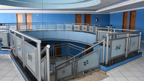 Atrio circolare con ringhiera in vetro, pareti blu e porte in legno.