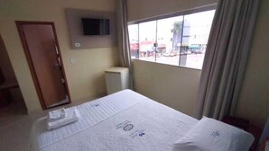 Una camera d'albergo con un letto, una TV a muro, una finestra con tende e una porta.