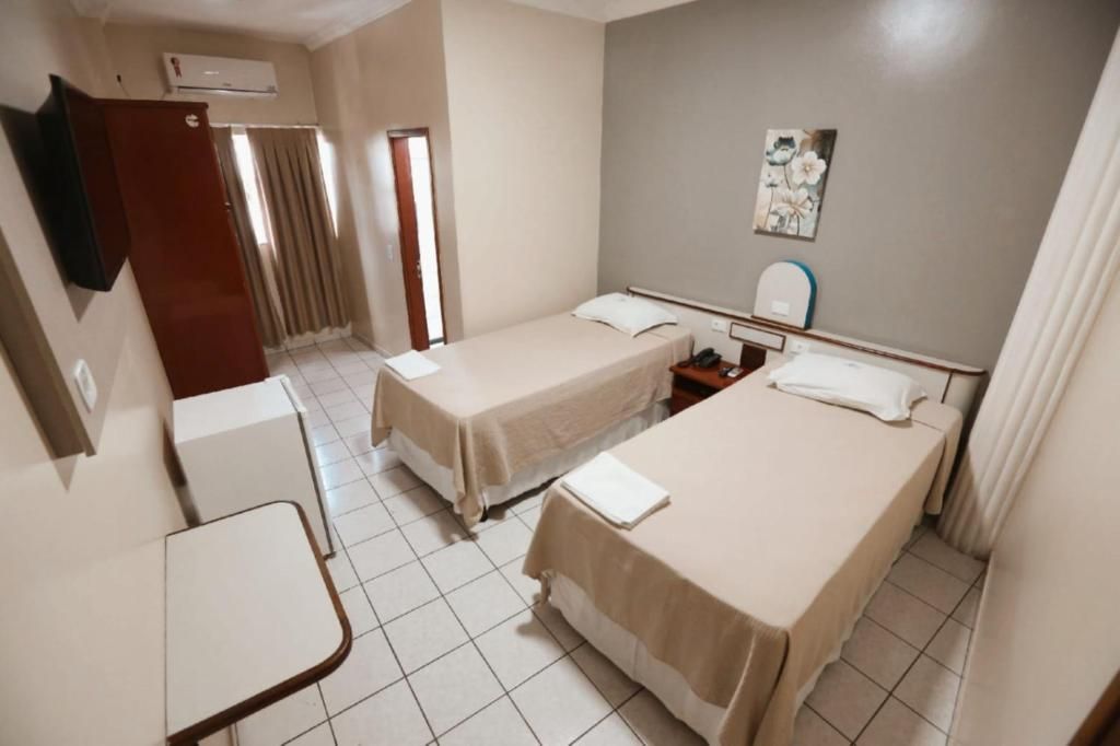 A hotel room with two single beds, a small table, a TV, and a window with curtains.