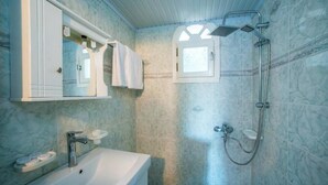 Een badkamer met een witte wastafel, een spiegel, een douche met een handdouche en een raam.