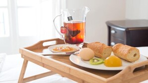 Een dienblad met een theepot, een bord met brood, een kiwi, een ei en een klein potje jam.