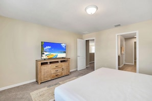Ein Schlafzimmer mit einem Bett, einem Fernseher auf einer Holzkommode und einer Tür zu einem anderen Raum.