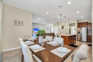 A dining room with a wooden table set for six, white chairs, and a 'EAT' sign on the wall.